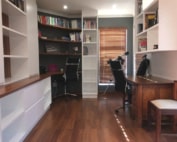 A home office with bookshelves, a wooden desk, and black office chairs.