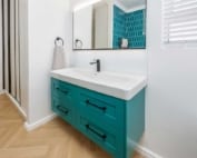 A modern bathroom with a turquoise vanity, a white countertop, a mirror above it, and a blue tile on the wall.