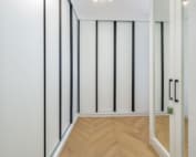 An empty room with white walls and black accents, featuring a mirrored surface and wooden flooring.