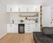 A modern living space featuring a white cabinet with shelves, a small fridge, and a sink, alongside a gray couch.