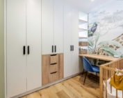 A modern nursery with white cabinets, a wooden desk, and a crib. The wall features a mural of a giraffe among foliage.